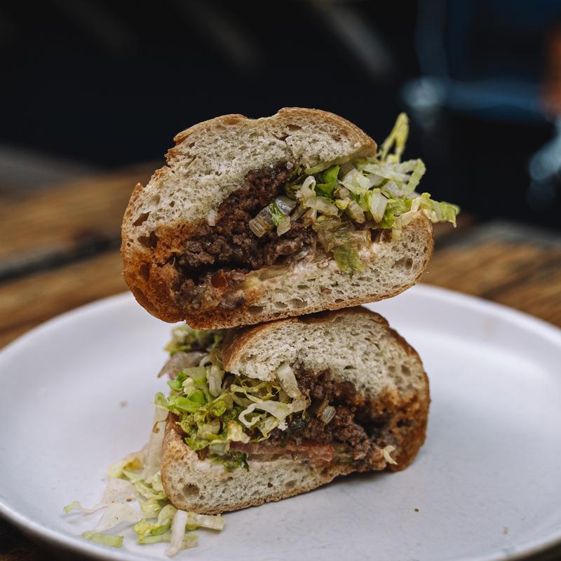 Ground beef sandwich, with onions, cheese, cheddar, lettuce, tomato, and aioli