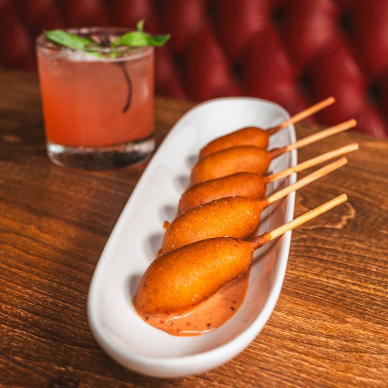 Mini corn dogs on a plate beside a cocktail