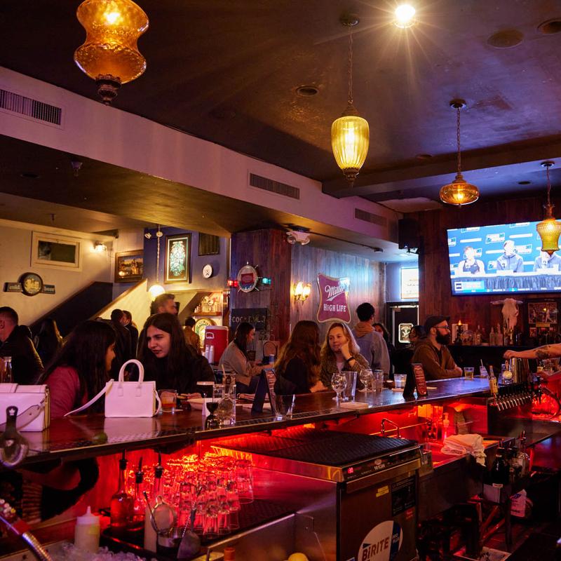 A crowded bar washed in red light, with a game on the TV