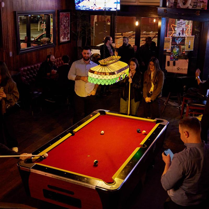 Guests shooting pool under a stained-glass lamp