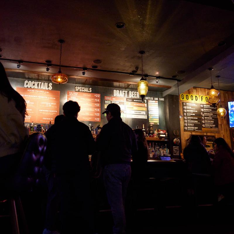 Guests at the bar under the cocktail, specials and draft beer boards