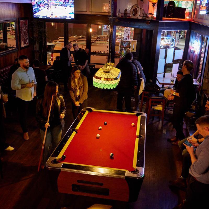 Guests around the pool table with games on the TVs