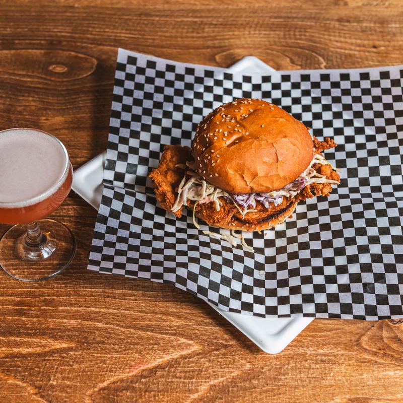 Fried chicken sandwich served on checkered paper next to a cocktail