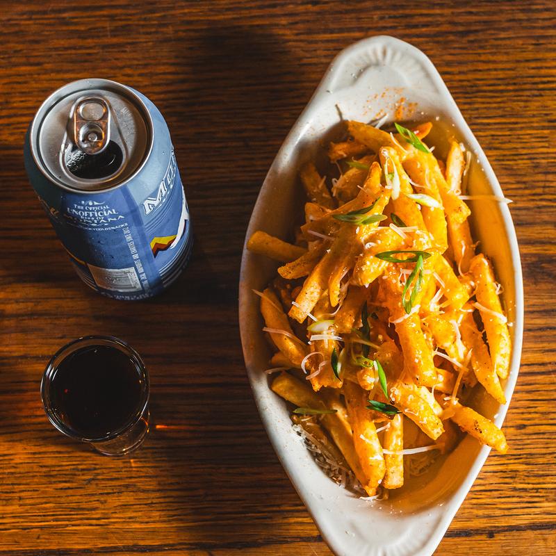 A bowl of fries on a table with a can of beer and a shot