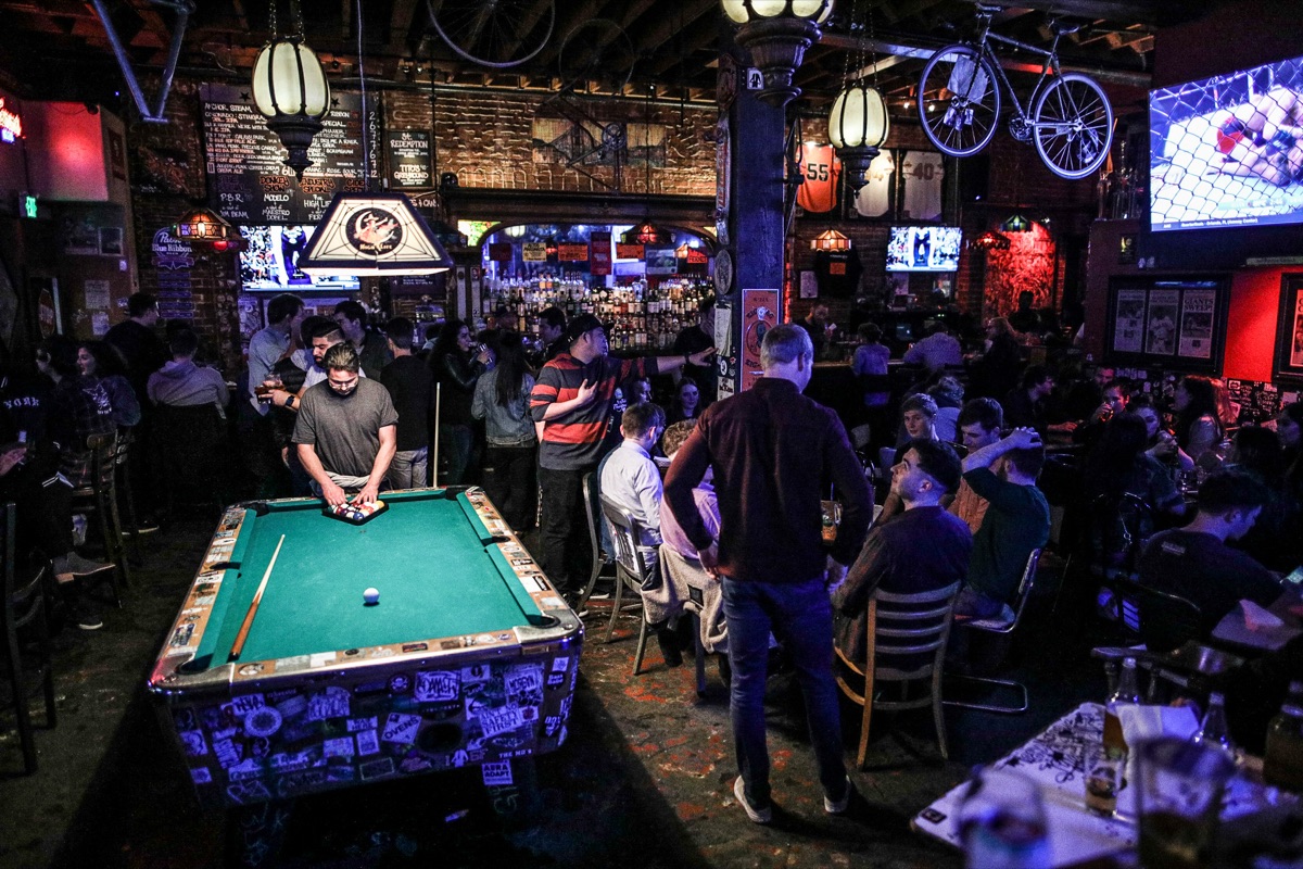 A pool game underway under the lamp, crowd deep behind the table