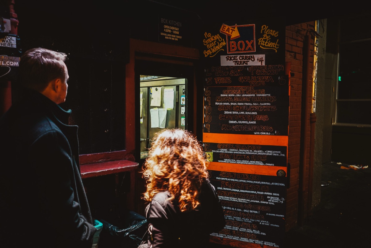 Two guests reading the chalk menu at the Box Kitchen ordering window inside Tempest