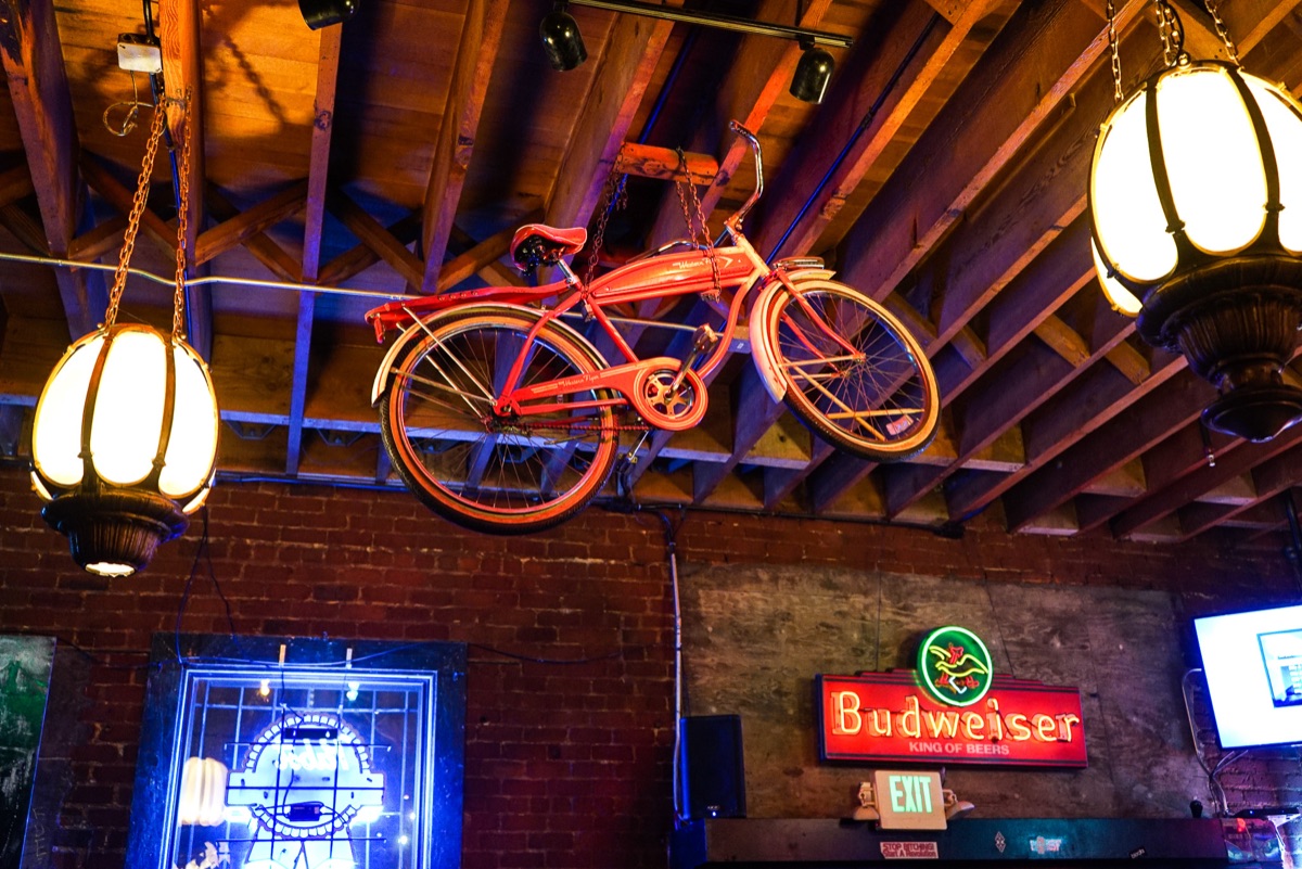 The orange bicycle hanging from the open-beam ceiling between lantern lamps